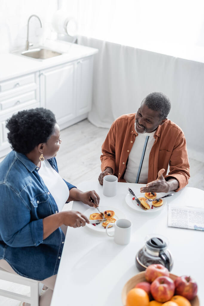 Blick aus der Vogelperspektive auf einen älteren afrikanisch-amerikanischen Mann, der während des Frühstücks mit seiner Frau spricht  - Foto, Bild