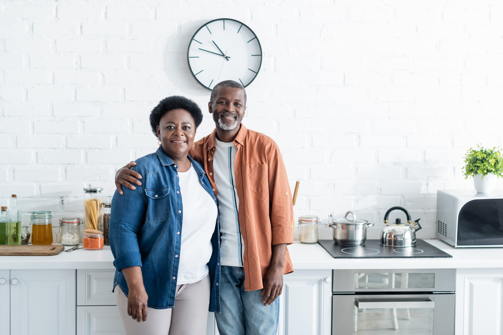 ευτυχισμένο ζευγάρι Αφροαμερικανών ηλικιωμένων που κοιτάζουν την κάμερα στην κουζίνα.  - Φωτογραφία, εικόνα