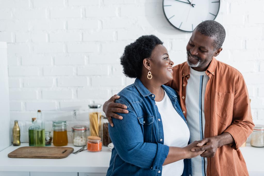 Χαρούμενος Αφροαμερικάνος που κοιτάζει τη γυναίκα του στην κουζίνα. - Φωτογραφία, εικόνα