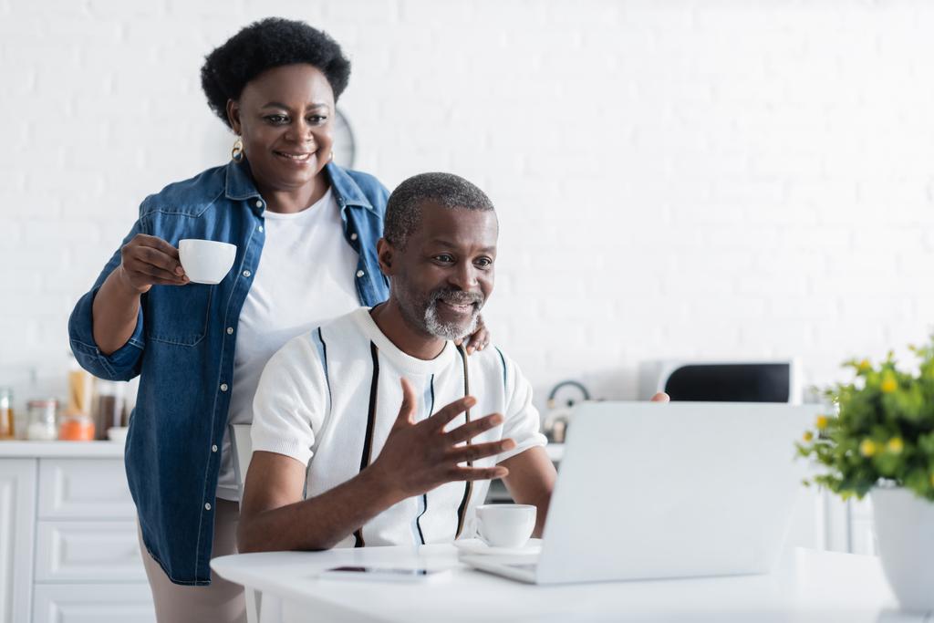 Üst düzey Afro-Amerikan adam görüntülü konuşma sırasında dizüstü bilgisayara bakarken karısının yanında el kol hareketi yapıyor. - Fotoğraf, Görsel