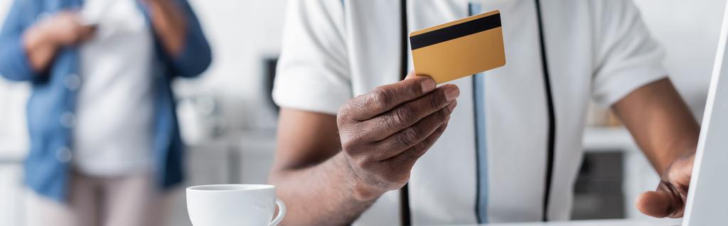 bijgesneden beeld van senior Afro-Amerikaanse man met credit card in de buurt beker, banner - Foto, afbeelding