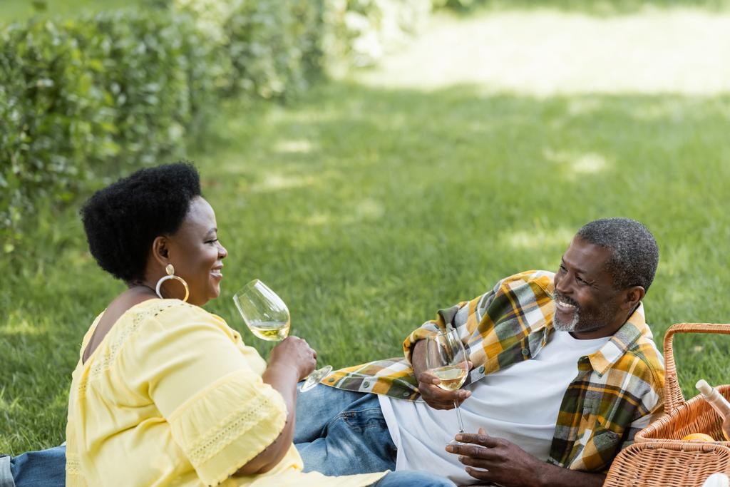 χαρούμενο και ηλικιωμένο αφροαμερικάνικο ζευγάρι που πίνει κρασί κατά τη διάρκεια του πικ-νικ  - Φωτογραφία, εικόνα