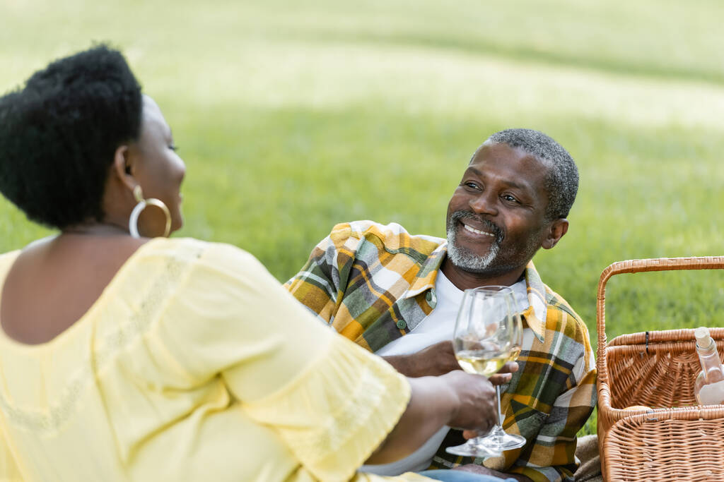 χαμογελαστό και ηλικιωμένο αφροαμερικάνικο ζευγάρι που κρατάει ποτήρια κρασί κατά τη διάρκεια του πικ-νικ  - Φωτογραφία, εικόνα