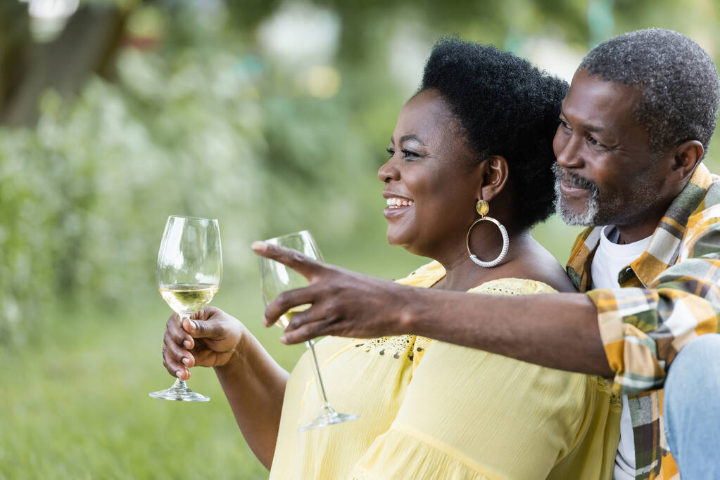 ρομαντικός ανώτερος Αφροαμερικάνος δείχνει μακριά κοντά ευτυχισμένη γυναίκα με ένα ποτήρι κρασί - Φωτογραφία, εικόνα