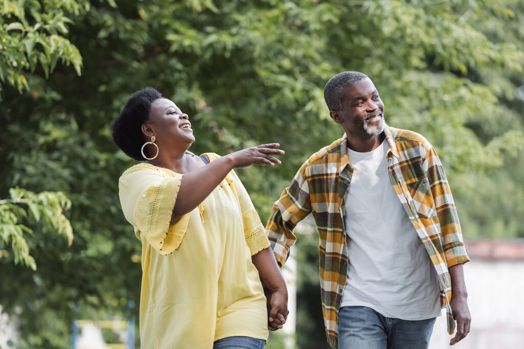 feliz adulto mayor afroamericano pareja cogido de la mano y caminando en parque - Foto, Imagen