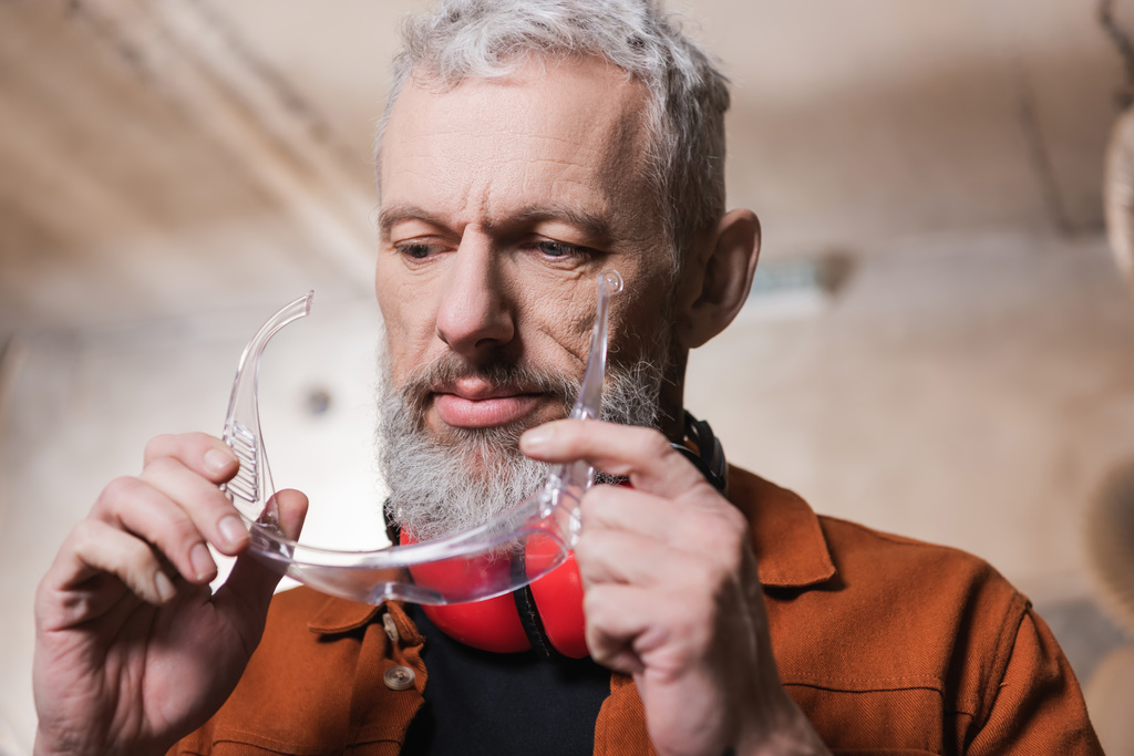 bearded middle aged furniture designer holding goggles in workshop - Photo, Image