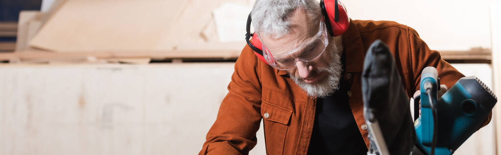 Orta yaşlı marangoz atölyede, pankartta testere başında çalışıyor. - Fotoğraf, Görsel