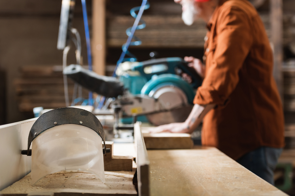 επιλεκτική εστίαση του προσώπου ασπίδα κοντά περικοπή ξυλουργός που εργάζονται σε θολή πριόνι μίτρα - Φωτογραφία, εικόνα