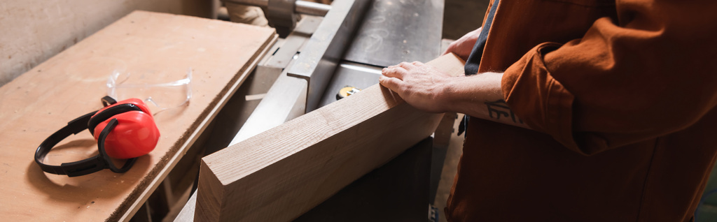 vista parcial del carpintero con el tablero cerca de orejeras de seguridad en el taller, pancarta - Foto, imagen