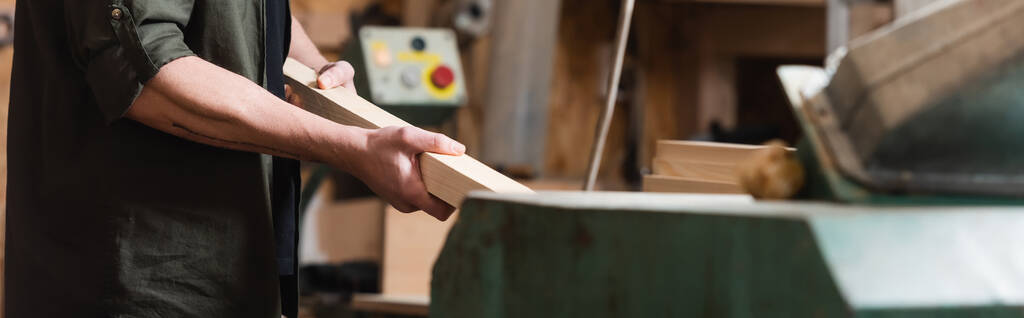 vue recadrée du designer de meubles tenant une planche en bois dans un atelier de menuiserie, bannière - Photo, image