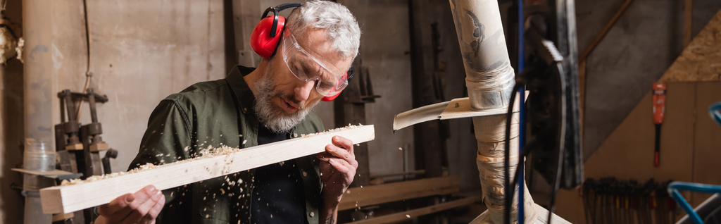 ξυλουργός με γυαλιά που φυσάει πριονίδι από σανίδα, λάβαρο - Φωτογραφία, εικόνα
