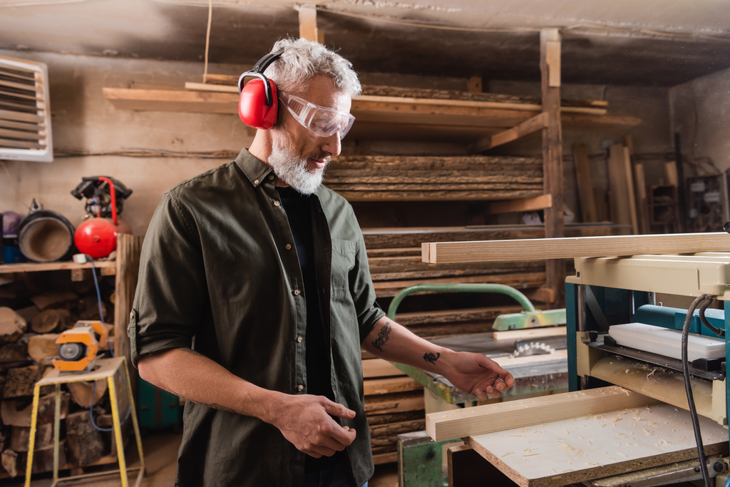 седой плотник, работающий в мастерской рядом с плотником толщиной - Фото, изображение