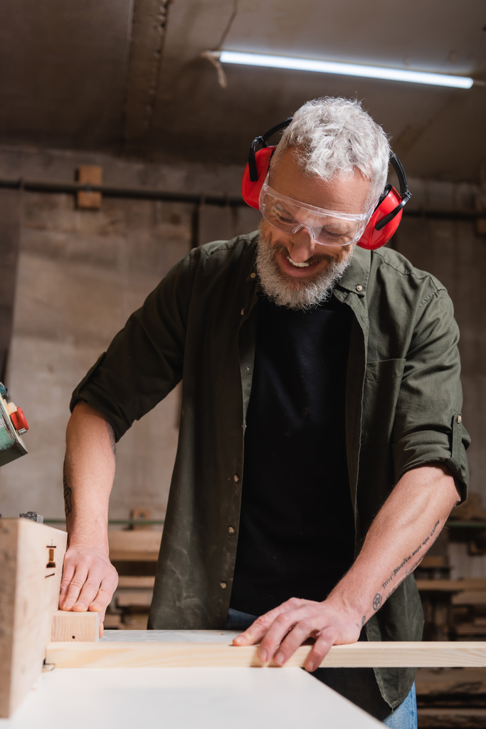 χαμογελαστός ξυλουργός σε γυαλιά εργασίας σε μηχανή Jointer στο εργαστήριο - Φωτογραφία, εικόνα