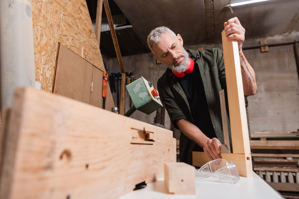 бородатый дизайнер мебели, измеряющий деревянный угол на размытом переднем плане - Фото, изображение