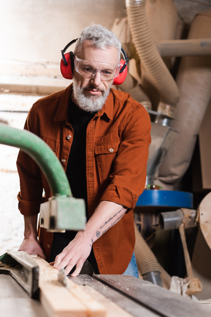 Tischler mittleren Alters arbeitet in Werkstatt an verschwommener Schreinermaschine - Foto, Bild