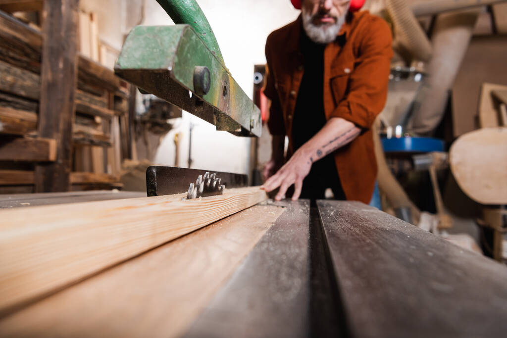 Çalışma tezgahının yüzey seviyesi dairesel testereyle bulanık arka planda kırpılmış marangozun yanında - Fotoğraf, Görsel