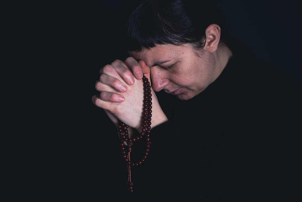Religiöse junge Frau betet vor dunklem Hintergrund zu Gott. - Foto, Bild