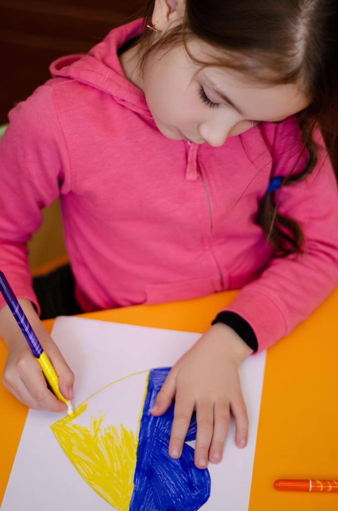 high angle view of kid drawing heart with ukrainian flag colors on yellow desk  - Photo, Image
