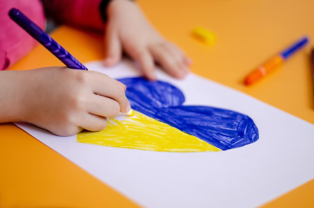cropped view of child drawing heart with ukrainian flag on yellow desk  - Photo, Image