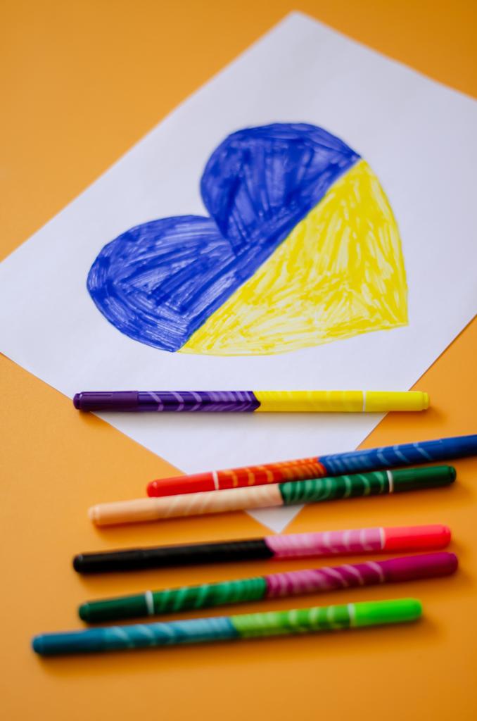 vista de ángulo alto de las plumas de fieltro cerca de papel con corazón dibujado y bandera ucraniana en amarillo  - Foto, imagen