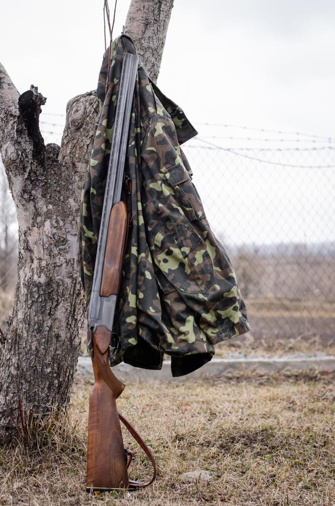 камуфляжна куртка біля гвинтівки в лісі
 - Фото, зображення