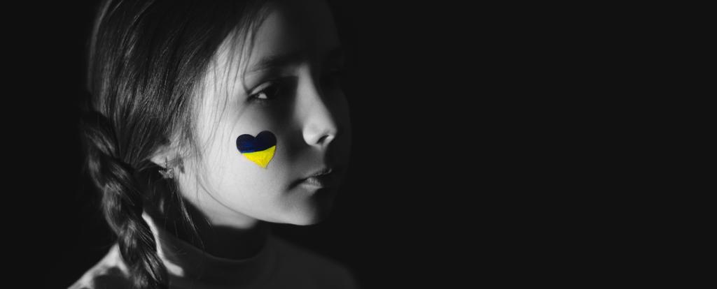 黒旗に描かれた頬にウクライナの旗を描いたフラストレーションのある少女のモノクロ写真 - 写真・画像