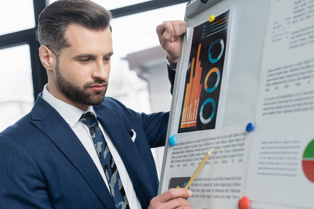 économiste pointant avec crayon vers les graphiques sur tableau à feuilles mobiles dans le bureau - Photo, image