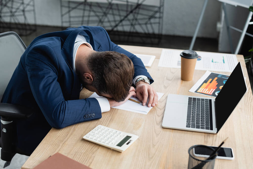 unavený ekonom spící na pracovišti v blízkosti kalkulačky a notebooku s prázdnou obrazovkou - Fotografie, Obrázek