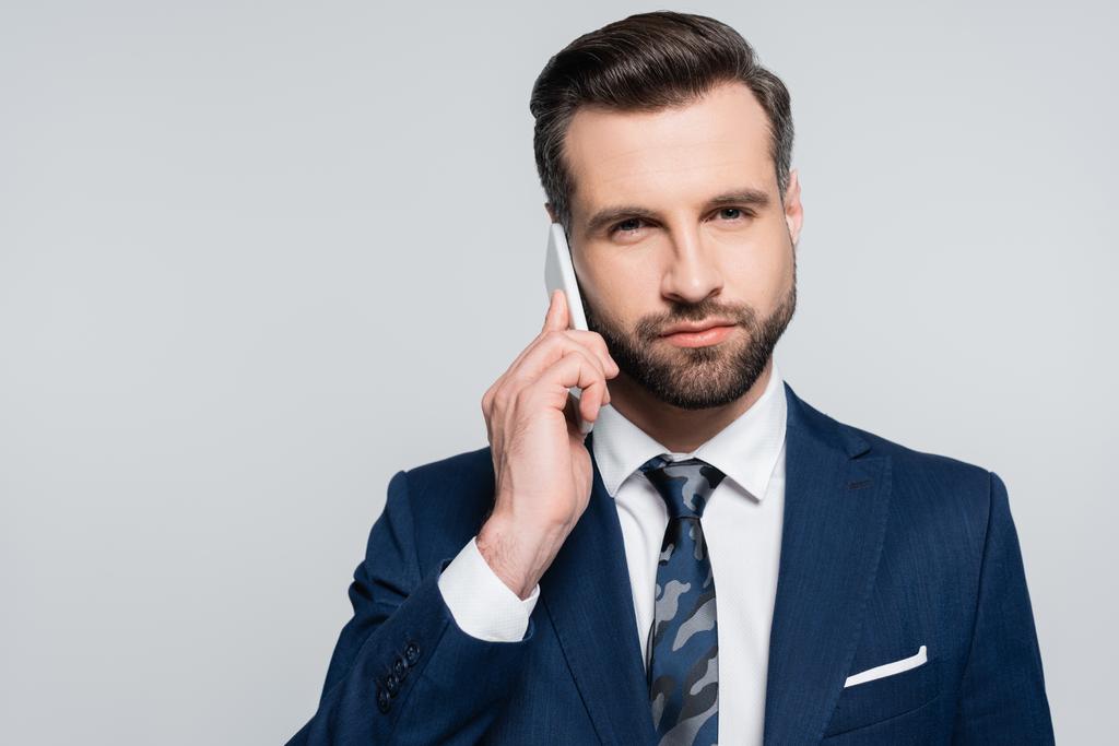 brunette businessman calling on mobile phone and looking at camera isolated on grey - Фото, изображение