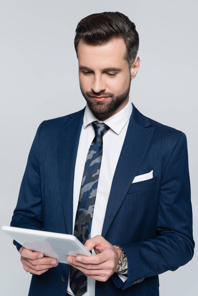 brunette economist in blue blazer using digital tablet isolated on grey - 写真・画像