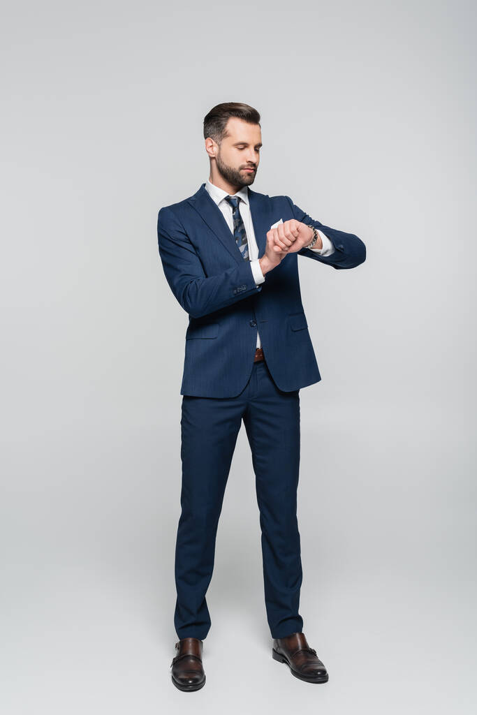 vista completa de hombre de negocios en traje azul comprobar el tiempo en gris - Foto, Imagen