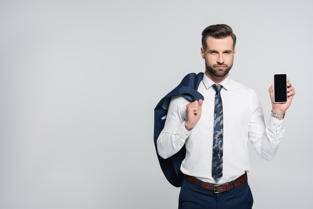 γενειοφόρος επιχειρηματίας κρατώντας σακάκι και smartphone με λευκή οθόνη απομονώνονται σε γκρι - Φωτογραφία, εικόνα