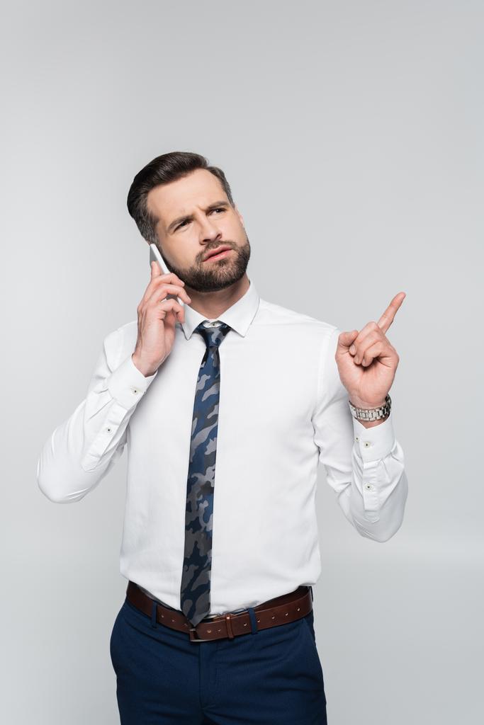 вдумчивый бизнесмен, говорящий по смартфону и указывающий пальцем на серый - Фото, изображение