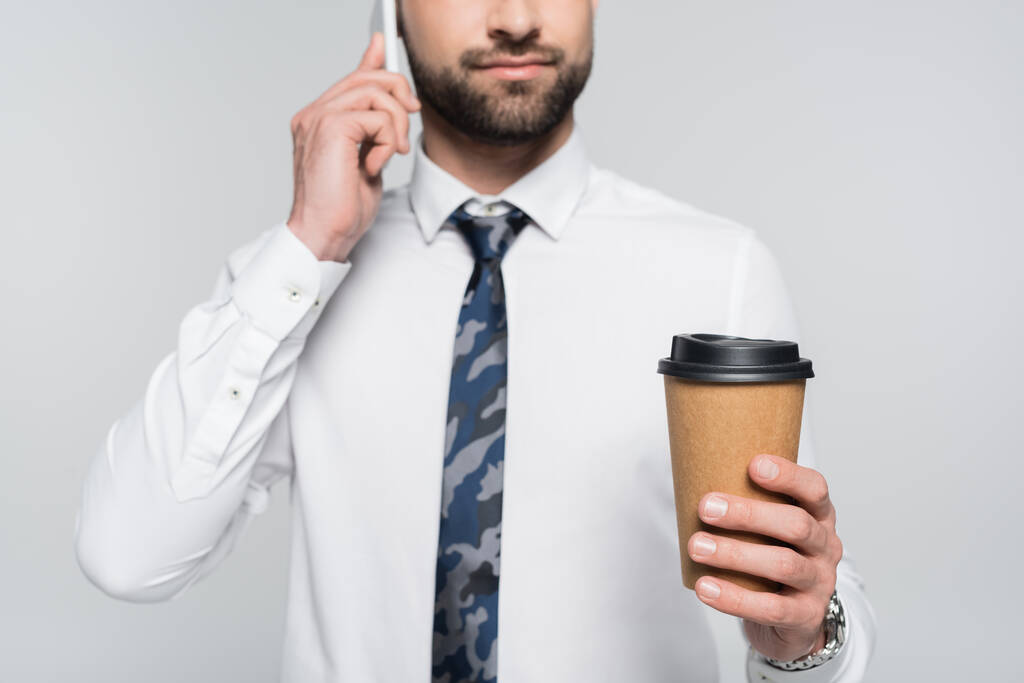 bijgesneden beeld van zakenman met koffie te gaan praten op mobiele telefoon geïsoleerd op grijs - Foto, afbeelding
