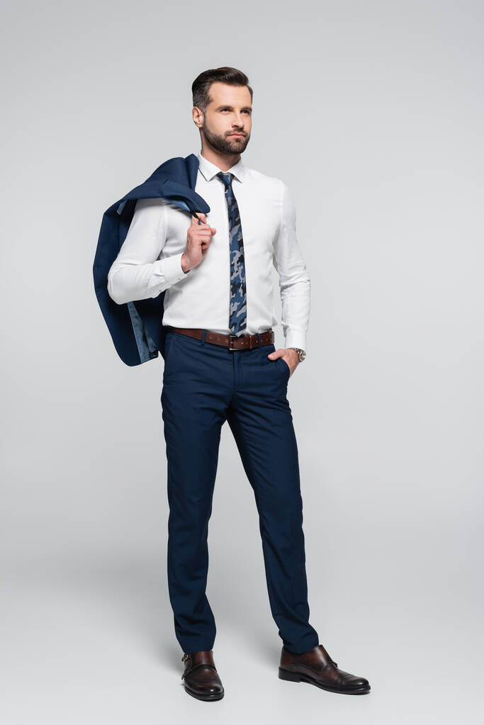full length view of confident businessman standing with hand in pocket on grey - Photo, Image
