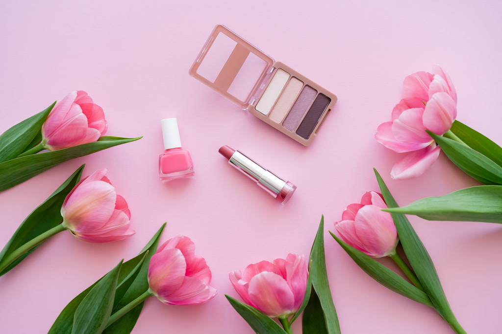 vrchní pohled na dekorativní kosmetiku v blízkosti kvetoucích tulipánů na růžové - Fotografie, Obrázek