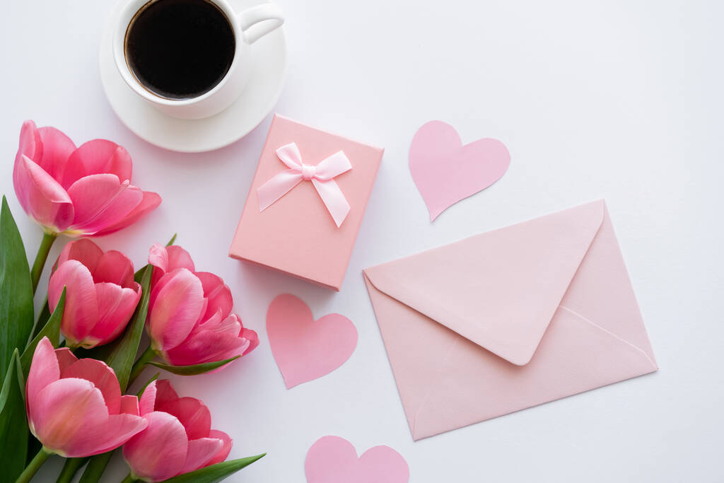 вид сверху на букет тюльпанов рядом с бумажными сердцами, конверт и подарочная коробка на белом - Фото, изображение