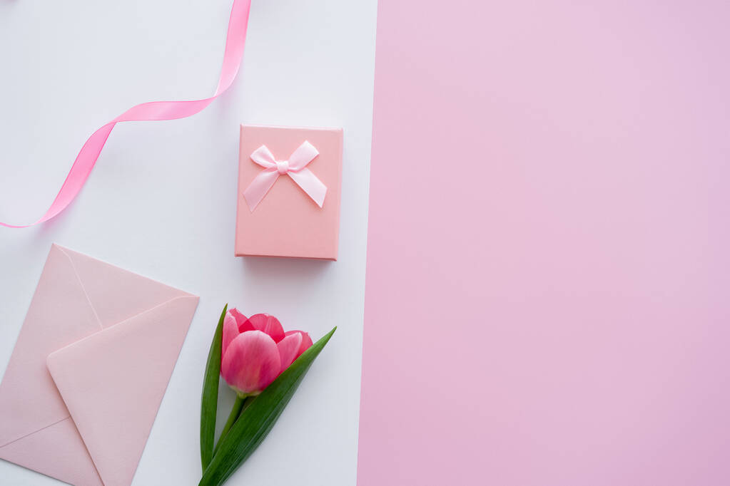 bovenaanzicht van enveloppe dichtbij geschenkdoos en tulp op wit en roze - Foto, afbeelding