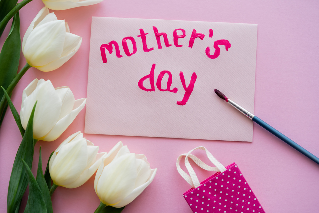 bovenaanzicht van penseel bij kaart met moederdag belettering en witte bloemen op roze  - Foto, afbeelding