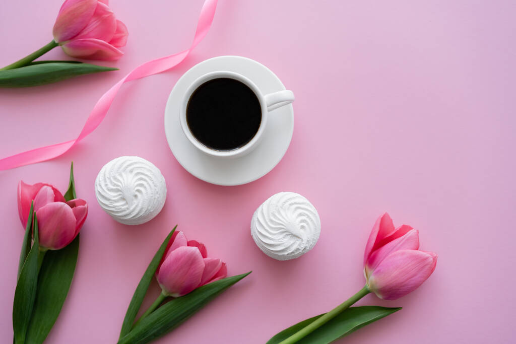 чашка с кофе рядом с зефиром, лента и тюльпаны на розовом  - Фото, изображение