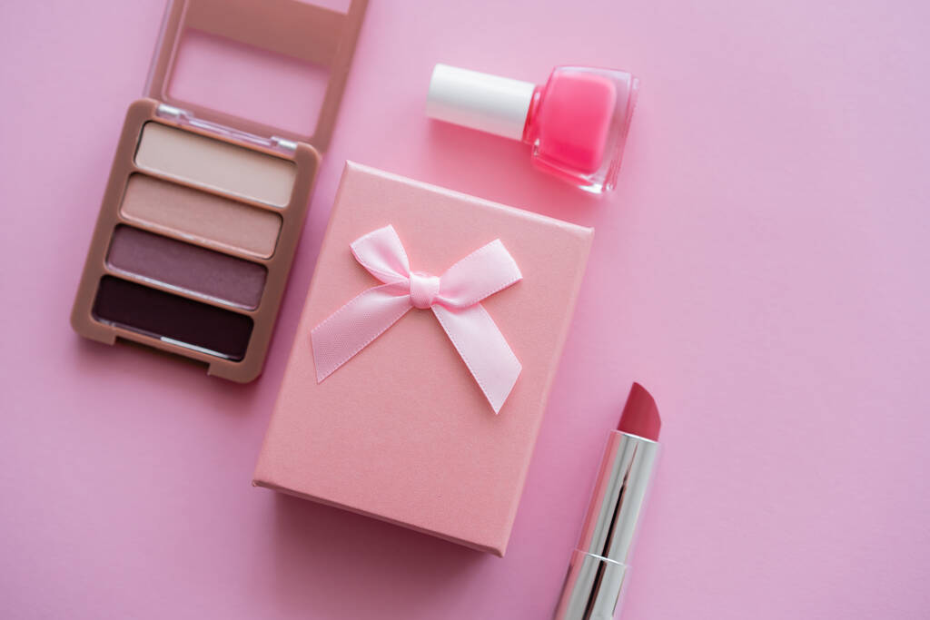 Ansicht der Geschenkbox mit Schleife in der Nähe von dekorativer Kosmetik auf rosa - Foto, Bild