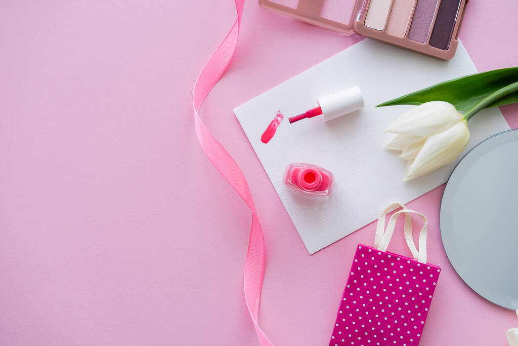 bovenaanzicht van penseelstreek van nagellak op kaart bij tulp en oogschaduw palet op roze  - Foto, afbeelding