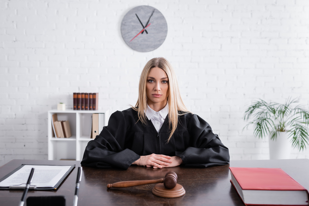 блондинка прокурор в мантии сидит за столом возле молотка и иск - Фото, изображение