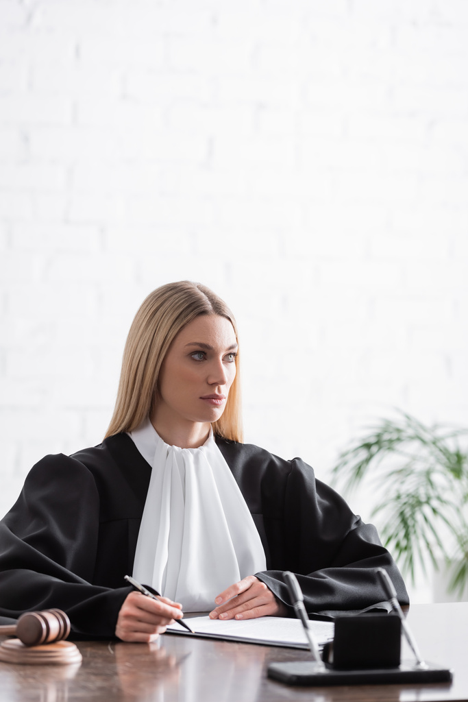 blond prokurátorka drží pero a dívá se jinam na pracoviště - Fotografie, Obrázek