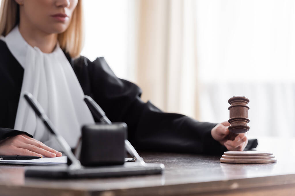 vista parcial del juez borroso sosteniendo el mazo mientras está sentado en el escritorio en la oficina - Foto, Imagen