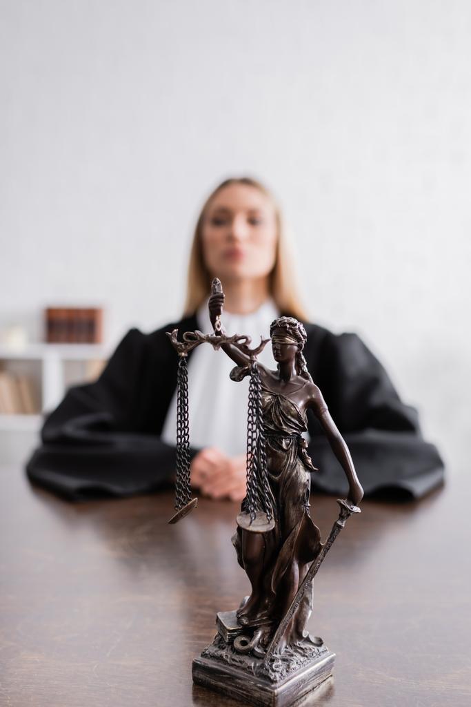 selective focus of themis statue near prosecutor in black mantle sitting on blurred background - 写真・画像