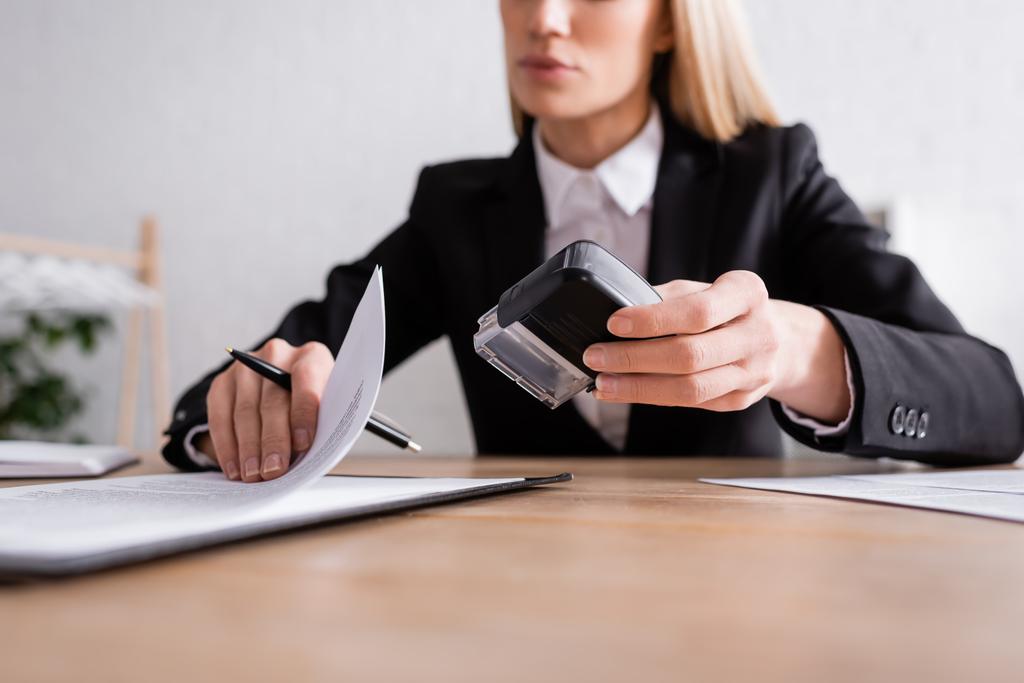 partial view of lawyer with pen and stamper working with contract on blurred background - Photo, Image