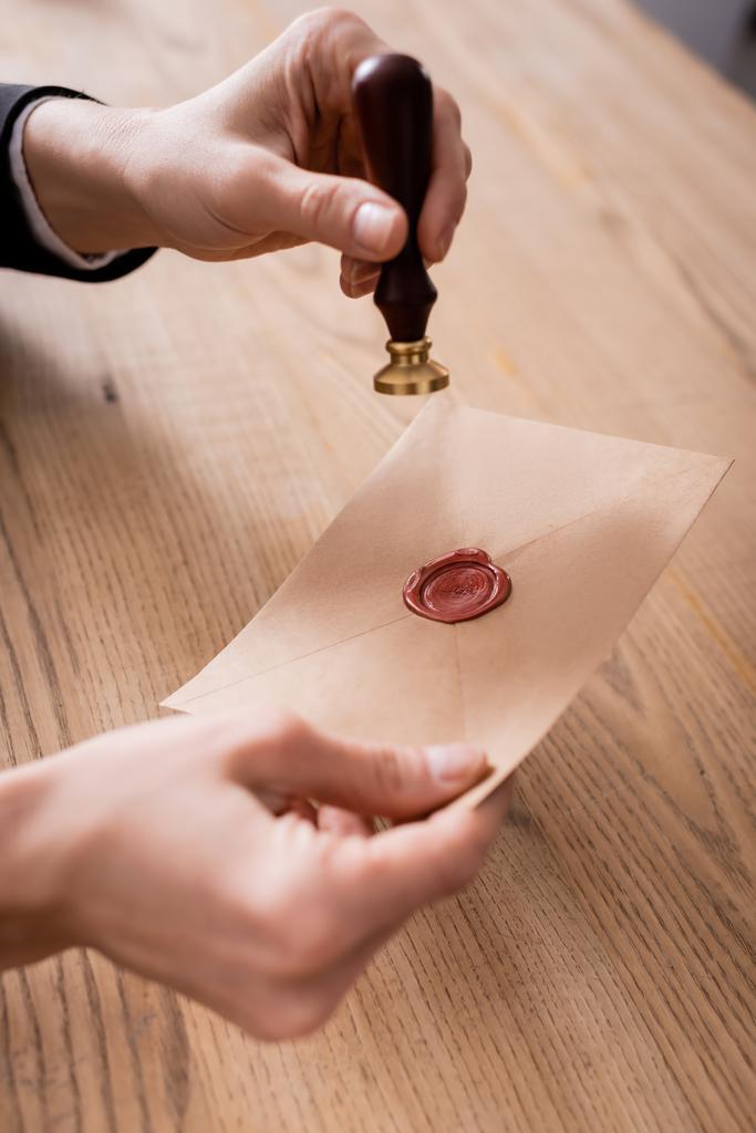 обрезанный вид нотариуса, держащего штамп и бумажный конверт с восковой печатью - Фото, изображение