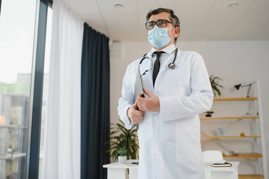 Άντρας γιατρός με μάσκα προσώπου και στηθοσκόπιο στην κλινική. - Φωτογραφία, εικόνα