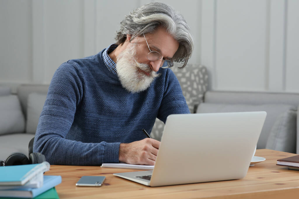 Középkorú férfi laptop és notebook tanulás asztalnál beltérben - Fotó, kép